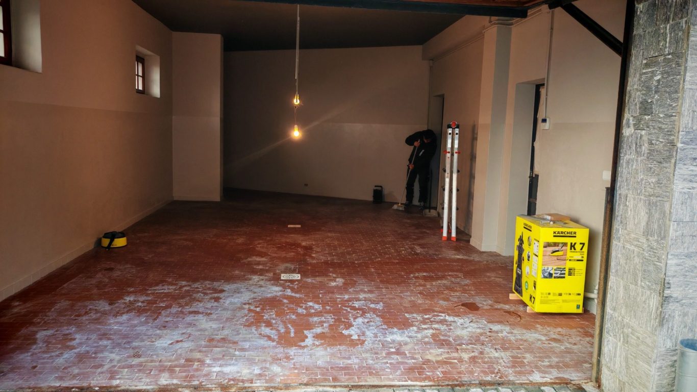 PRIMA Spacious, empty room with red flooring, a worker, and two pendant lights.